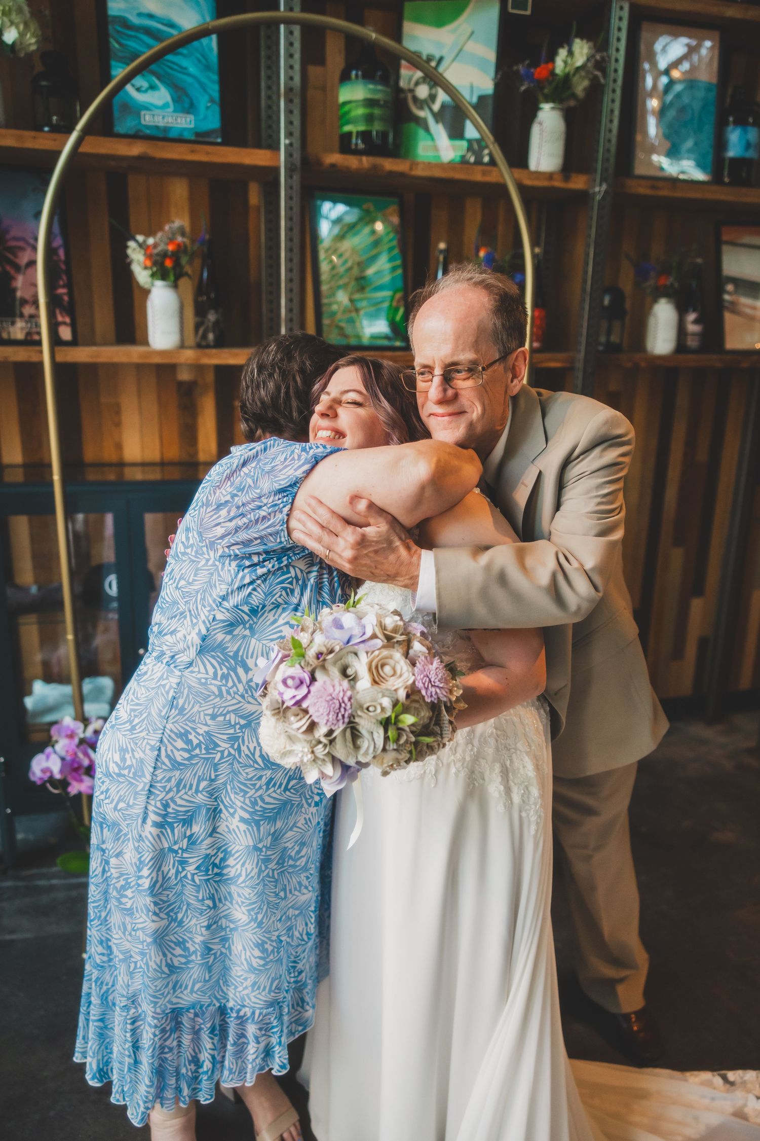 Emotional embrace during wedding ceremony with floral bouquet and decorative wooden backdrop.