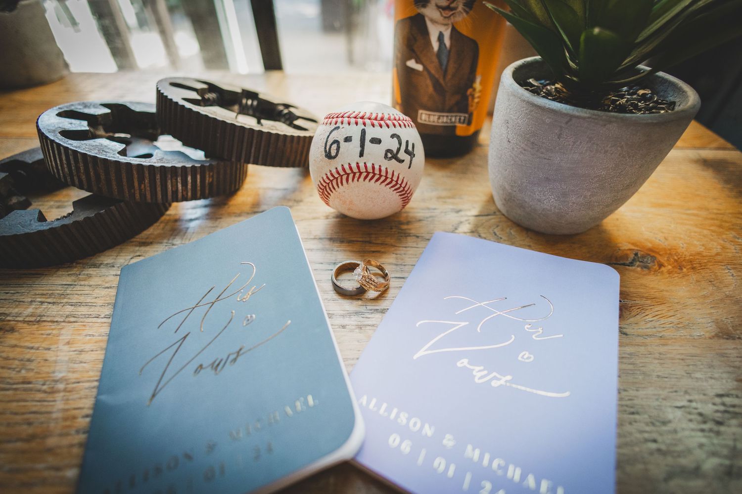 Wedding details including rings, a baseball, and blue invitation cards arranged on a wooden surface.