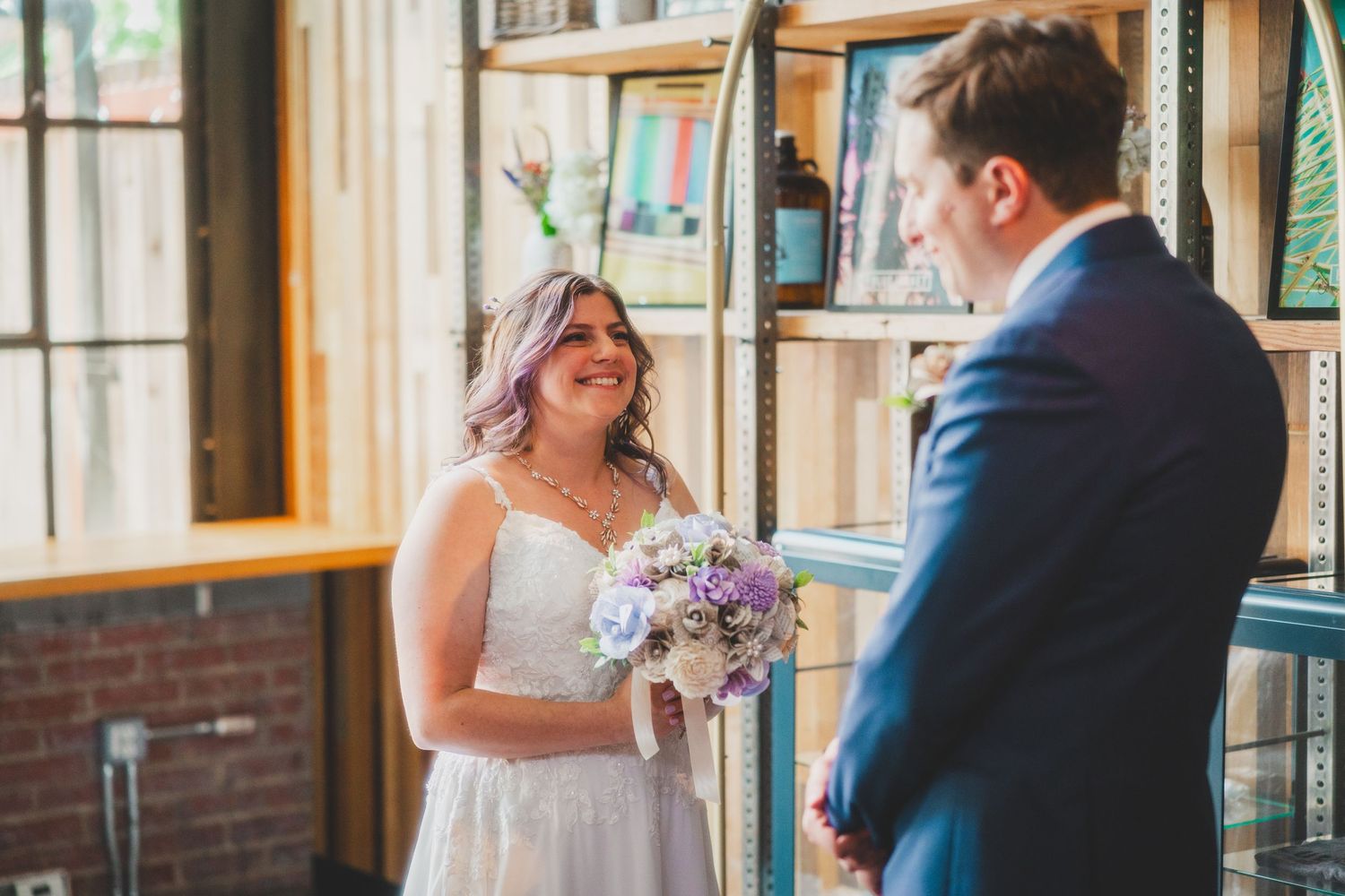 Wedding couple shares emotional moment during ceremony with shelving and brick wall backdrop.