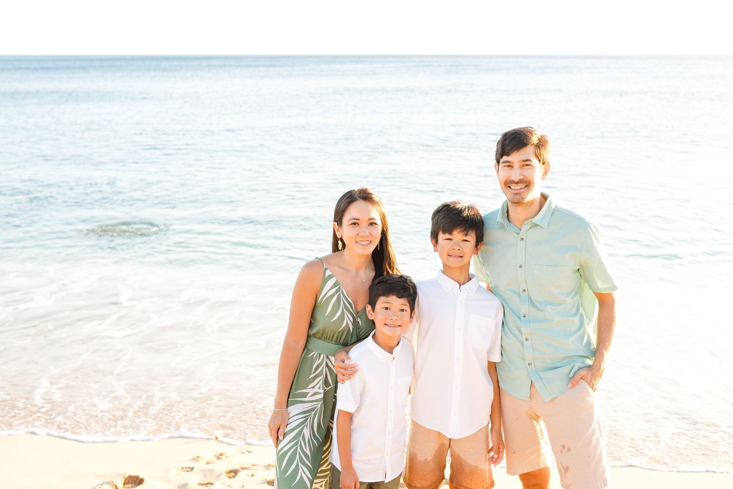 Family portrait on sunny beach with ocean waves in background. Oahu Family Photographer