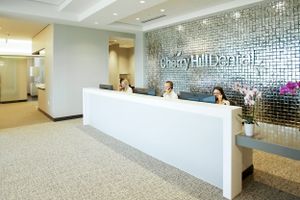 Modern dental office reception area with sleek white counter and metallic wall design featuring elegant decor and lighting.