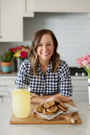 Bright kitchen scene with gingham shirt, freshly baked cookies and yellow lemonade on wooden board.