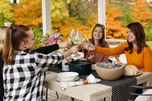 Friends toasting wine glasses during an autumn outdoor gathering with fall foliage in background.