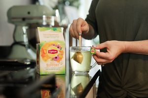 Hands preparing a beverage with a box of Lipton tea and mixer in the kitchen.