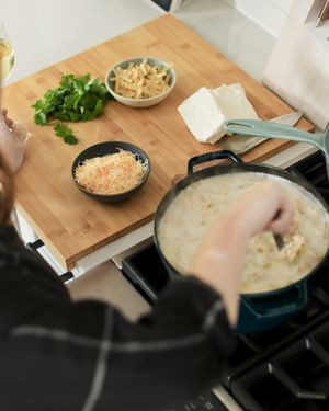 Cooking ingredients and pan on wooden cutting board with creamy sauce being prepared.