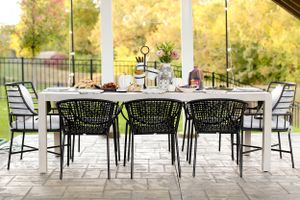 Empty outdoor patio dining set with black chairs against autumn background.