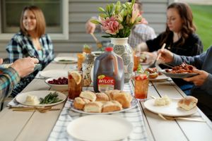 Casual outdoor dining scene with flowers, drinks and bread on a wooden table.