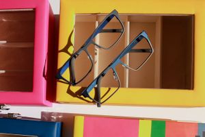 Black rimmed glasses displayed on colorful yellow and pink storage boxes.