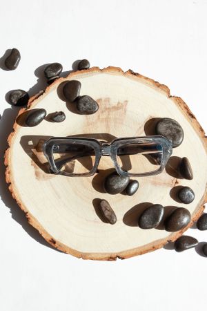 Black-rimmed glasses placed on a wooden slice with decorative dark stones.