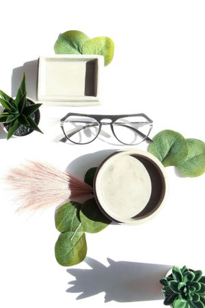 Modern eyeglasses arranged with succulents and green leaves on a white surface.