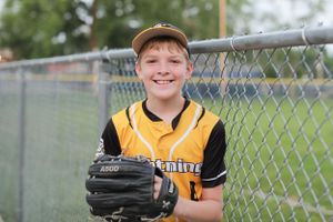 Baseball player in yellow uniform posing with glove against chain link fence.