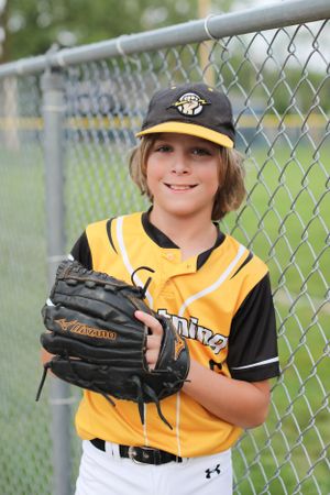 Youth baseball player in yellow and black uniform holding baseball glove by fence.