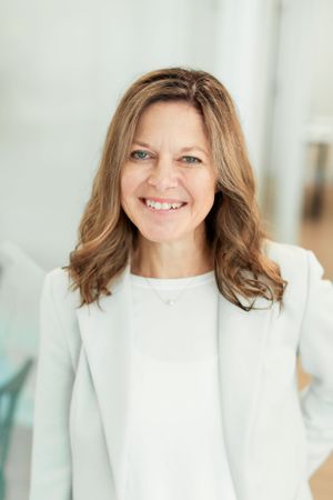 Professional portrait against a light background wearing a classic white top.