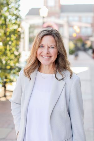 Outdoor professional portrait showing warm smile and light gray blazer against brick building.