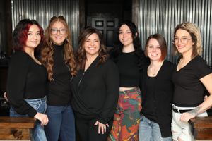 Group of six team members in casual attire posing together against dark background.