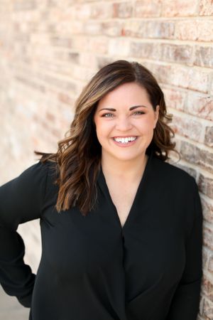 Professional headshot against brick wall background wearing black blazer.