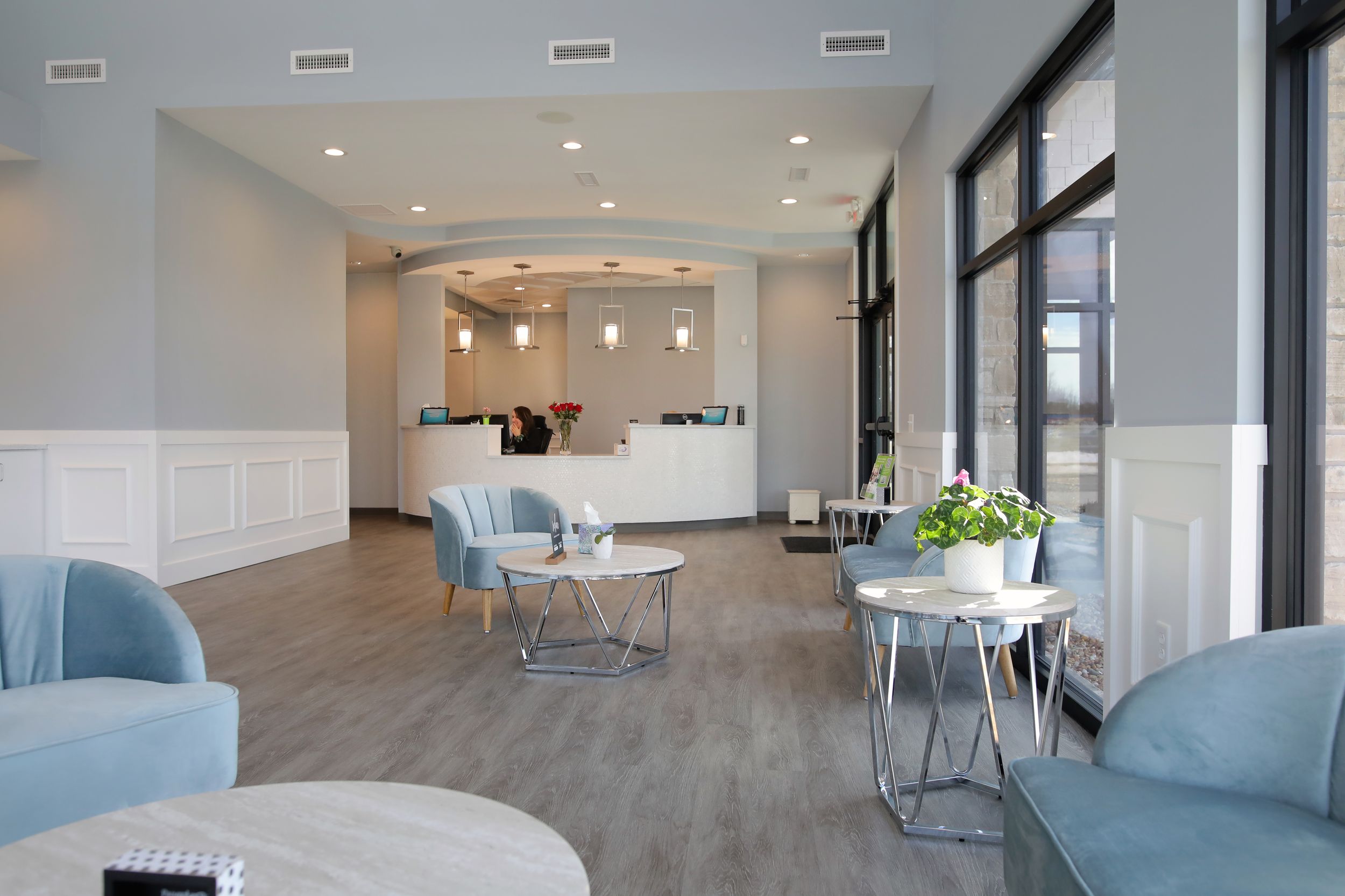 Modern waiting room with blue accent chairs, wood flooring, and large windows.