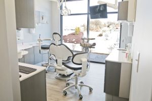 Modern dental office interior with white dental chair and equipment in clean clinical setting.