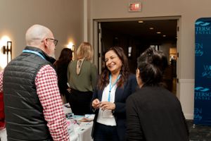 Networking event scene with people engaging in conversation near display table.