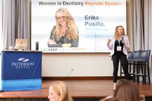 Presenter speaking at a Women in Dentistry event with presentation slides displayed behind them.
