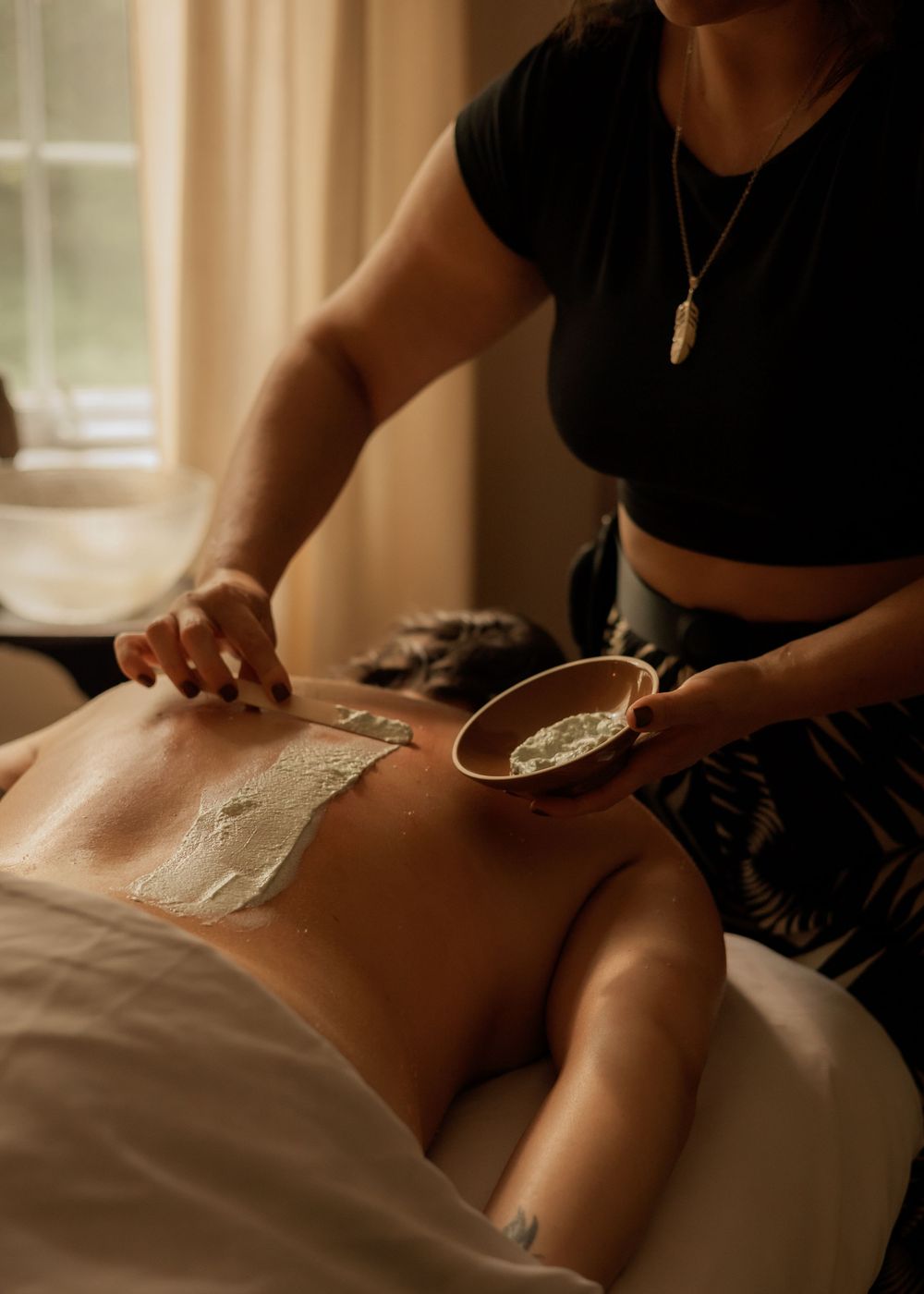 Professional massage therapist applying scrub treatment to client's back on massage bed.
