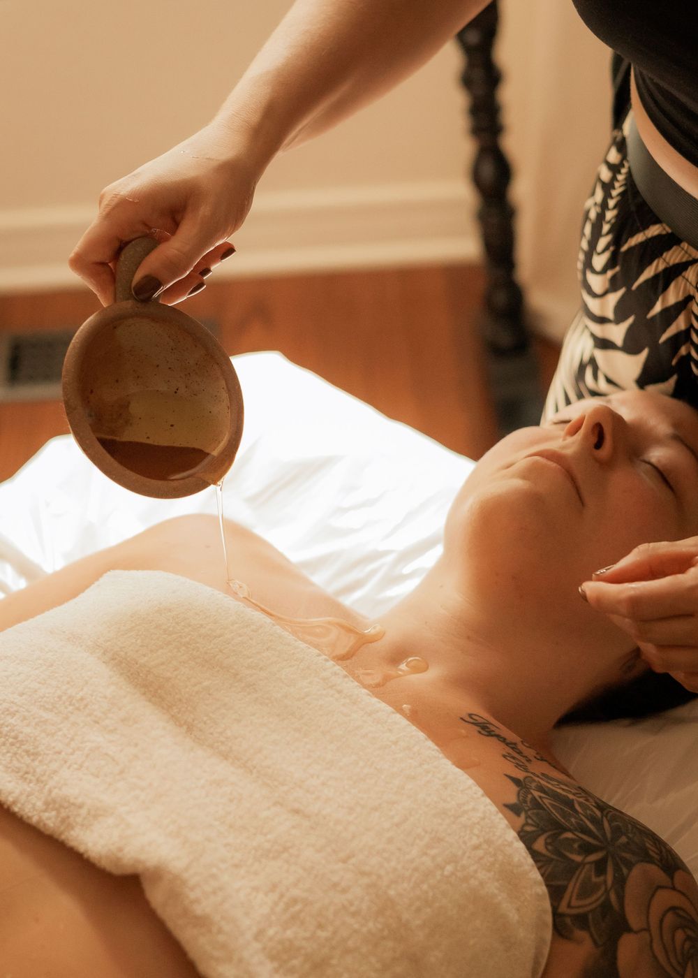 A massage therapist pouring oil during a relaxation treatment at a spa with warm lighting and white linens.