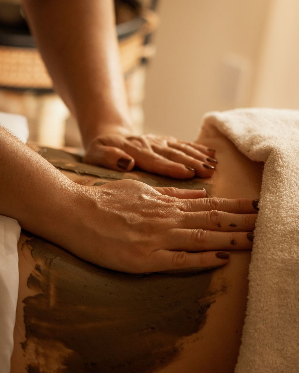 Hands performing a therapeutic massage treatment on a client covered with white towels in a spa setting.