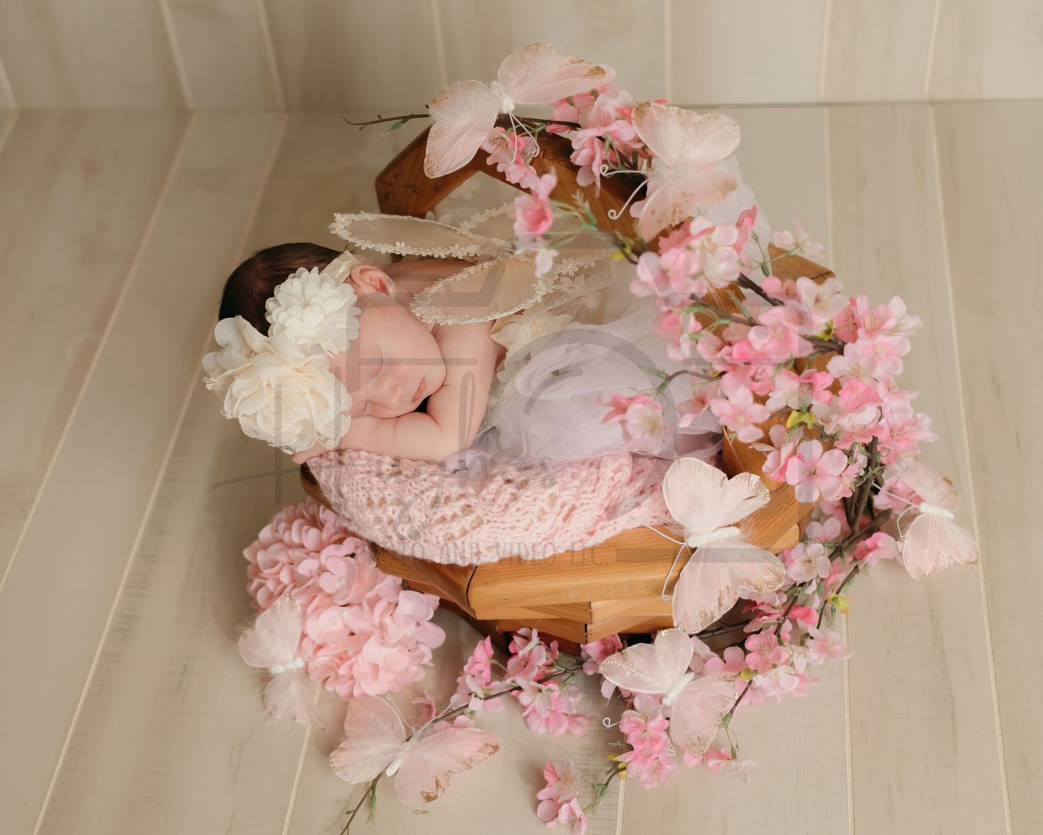 Delicate newborn photography setup with pink flowers and wooden basket.
