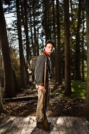 Civil War soldier with backpack and rifle glances back on forest wooden platform.