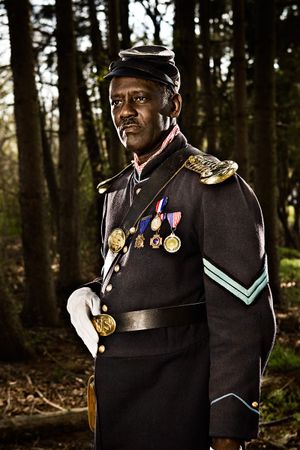 Decorated African American Union soldier in dress uniform with medals stands in forest.