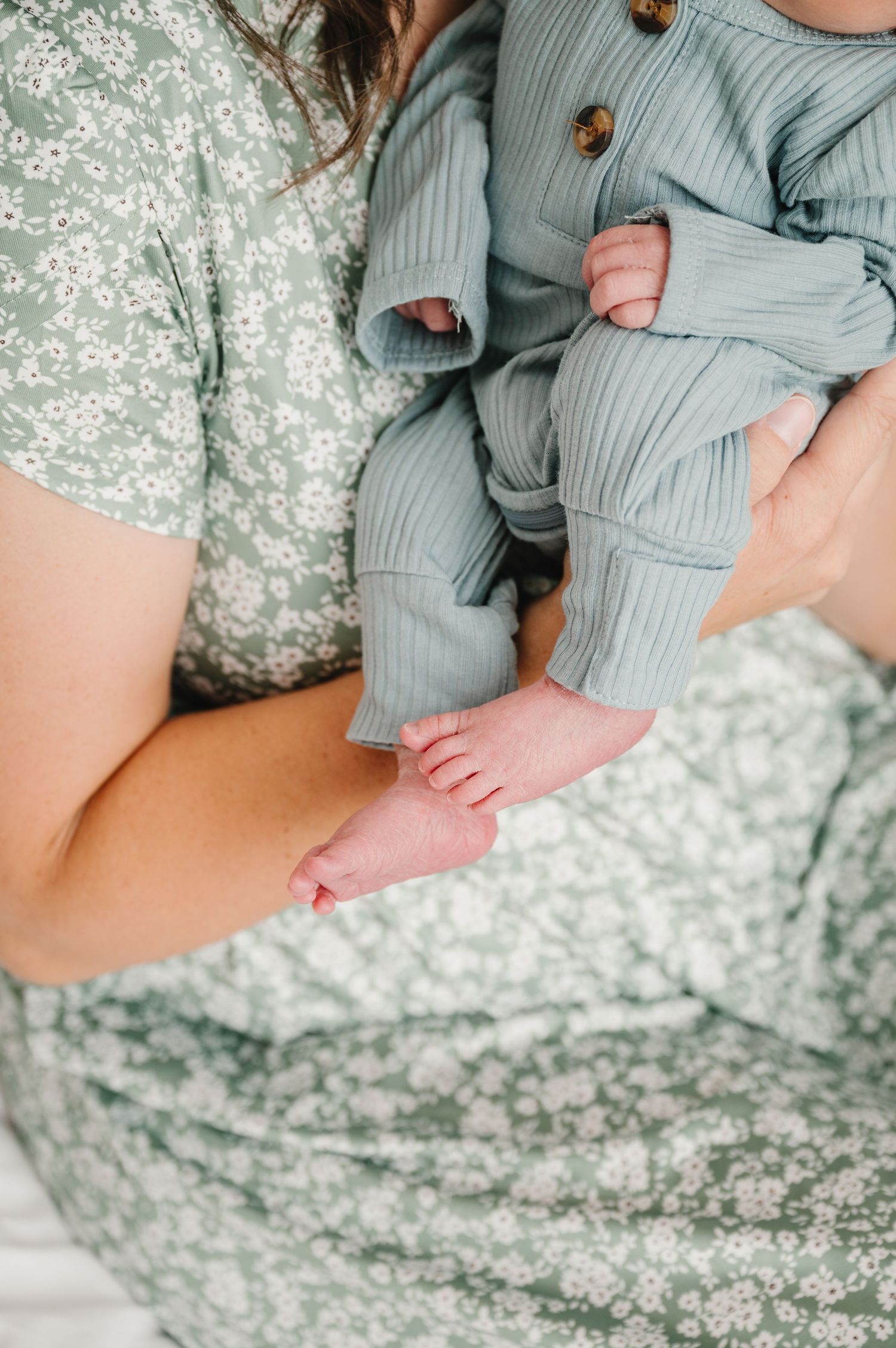 Close-up of tiny baby feet in blue ribbed clothing against a floral print fabric.