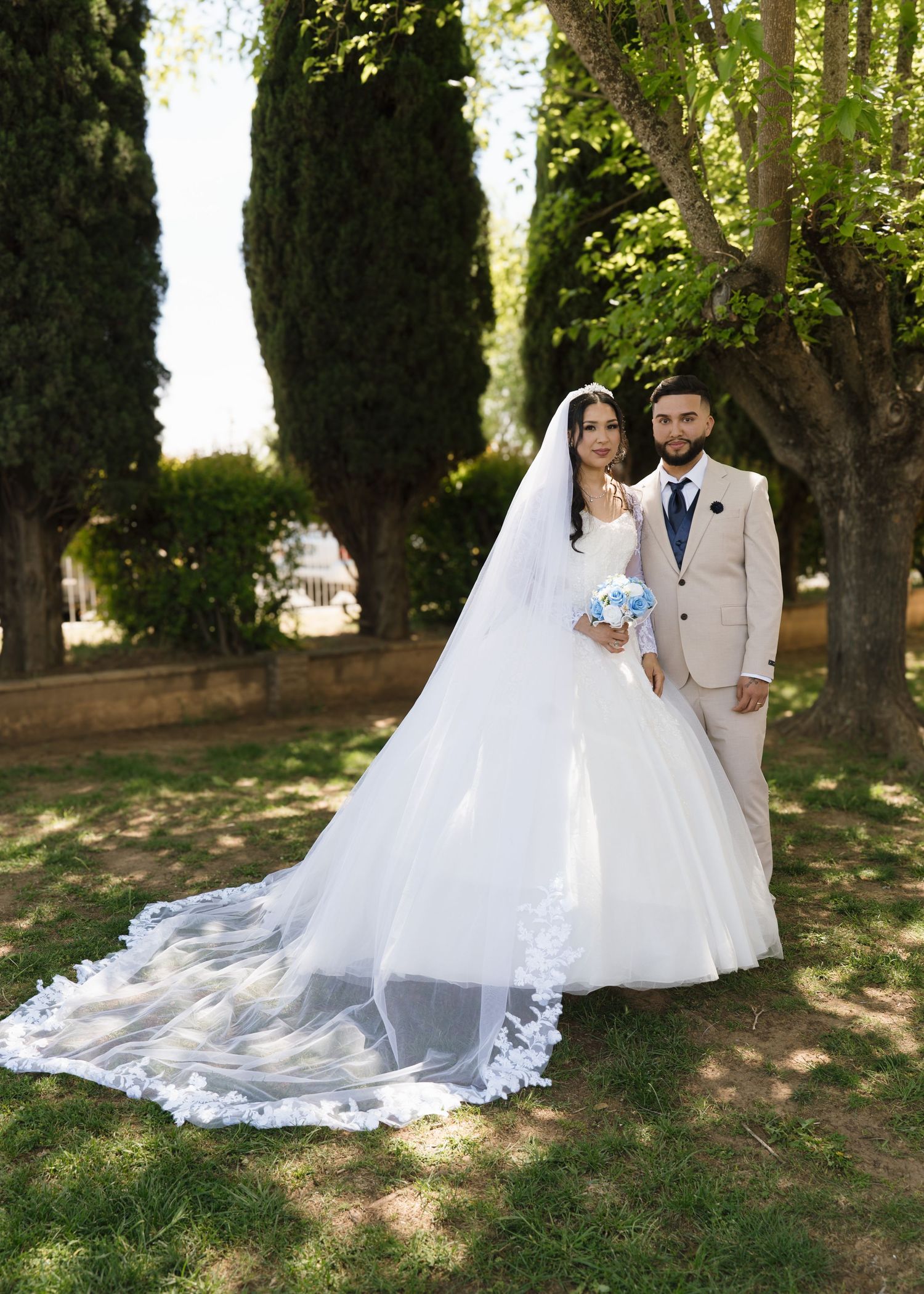 Bride in elegant white lace ball gown with veil and tiara poses gracefully at indoor wedding reception.
