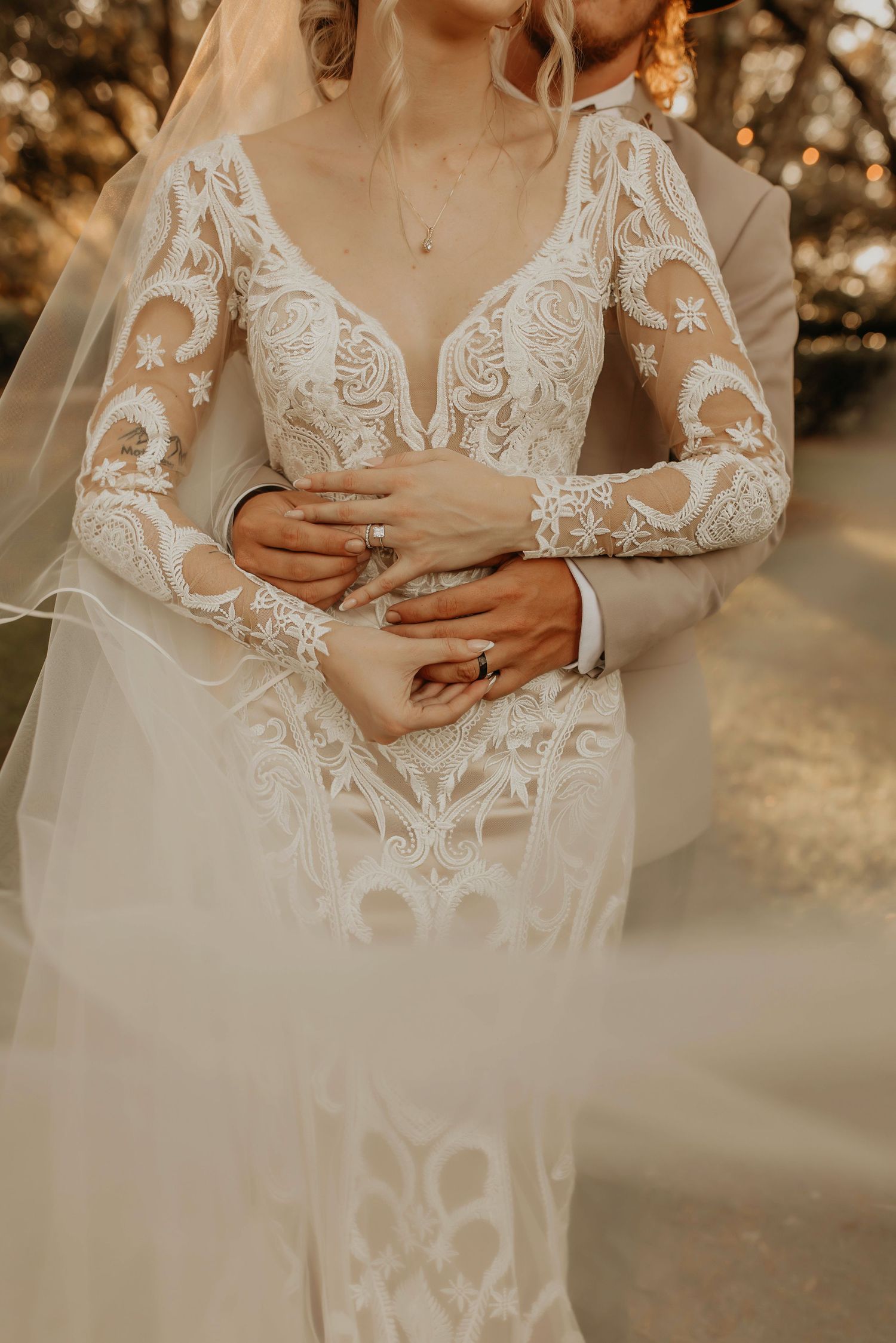 Detail shot of an elegant lace wedding dress with long sleeves in golden hour lighting.