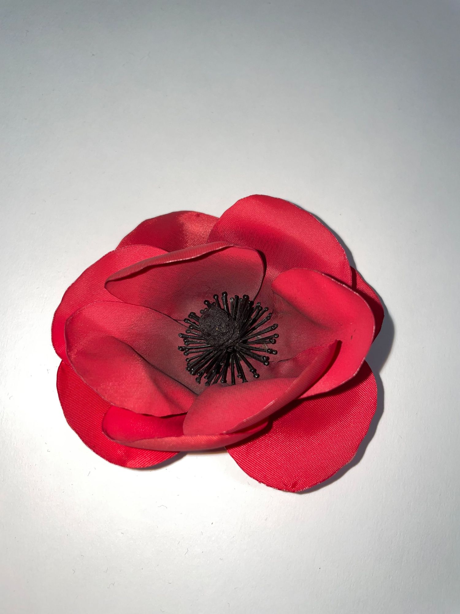 A vibrant red poppy flower with black center made from fabric or paper.