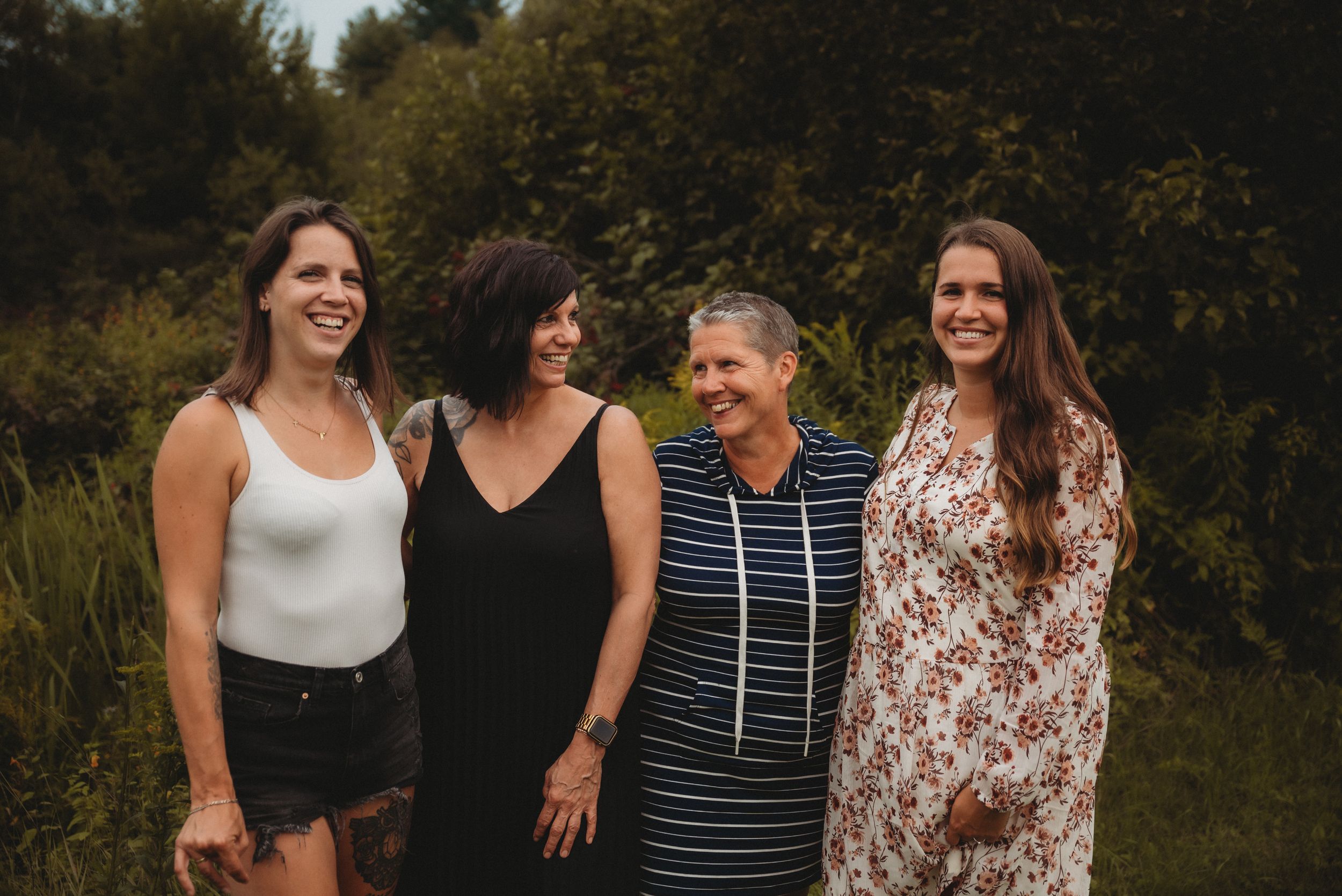 Four women standing together outdoors on a sunny summer day.