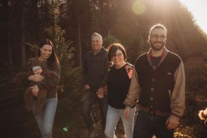 Family portrait in a forest setting with evergreen trees during golden hour.