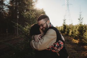 Couple embracing outdoors in a forest during golden hour with sunlight peeking through the trees.