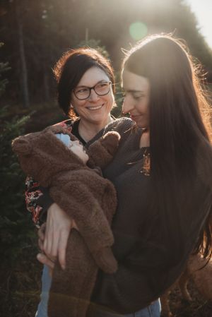 Two people share a joyful moment while holding a dog wrapped in a cozy brown blanket.