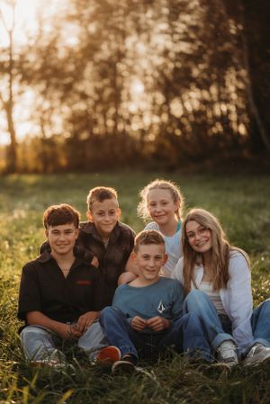 Group sitting together casually in a grassy field backlit by warm sunset light.