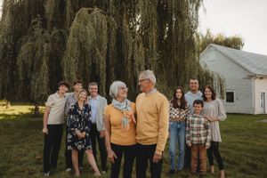 Extended family gathering under a majestic weeping willow tree beside a white house.