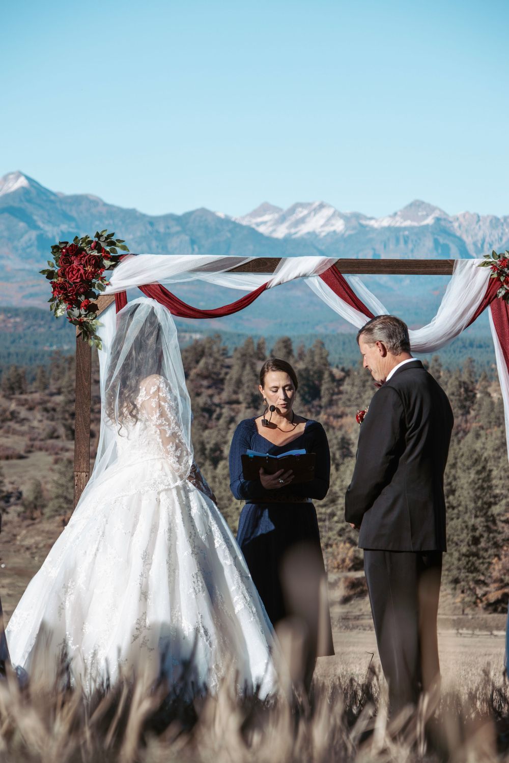 Outdoor wedding ceremony under draped arch with mountain landscape backdrop.