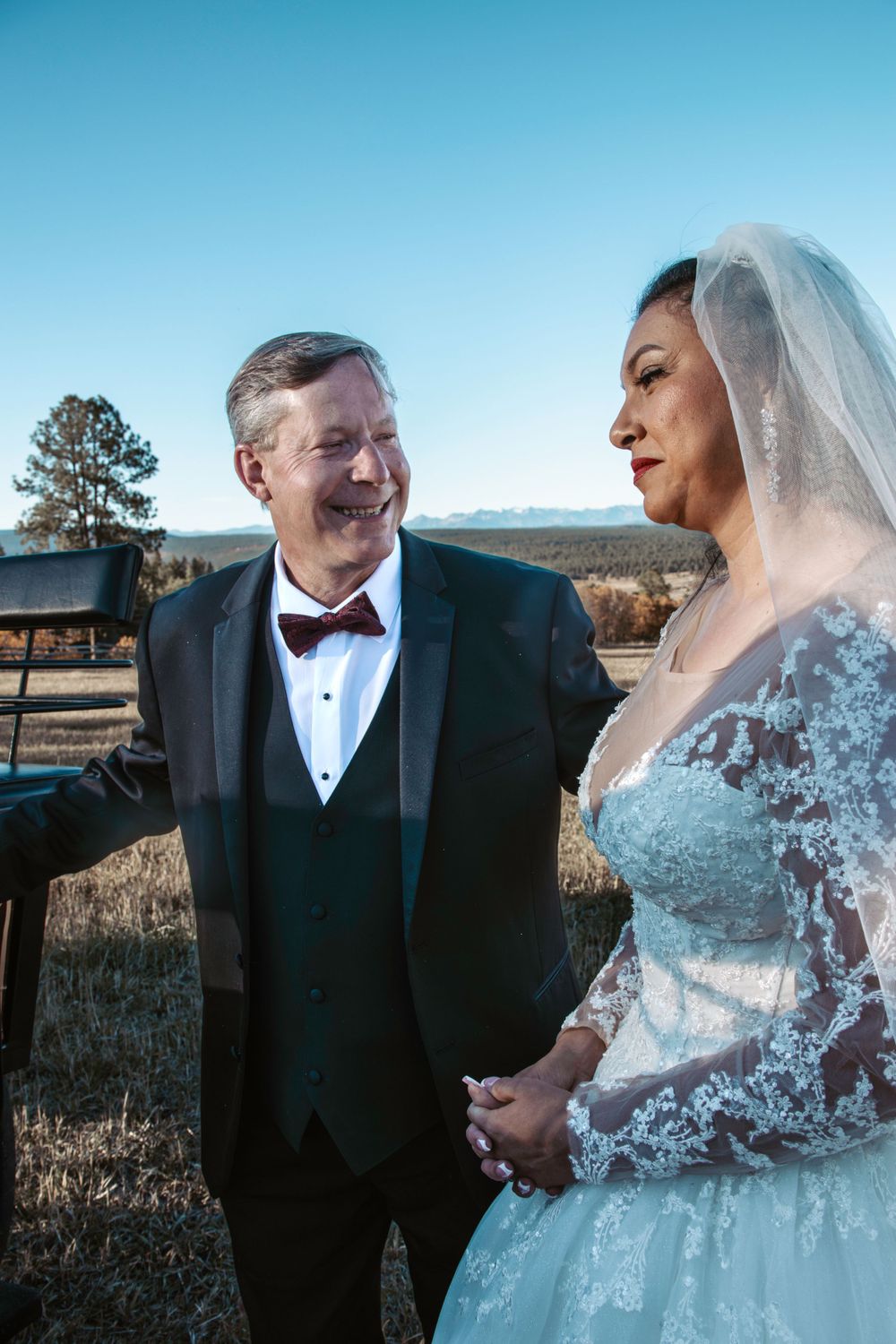 A bride and groom share a joyful moment outdoors against a scenic rural backdrop.