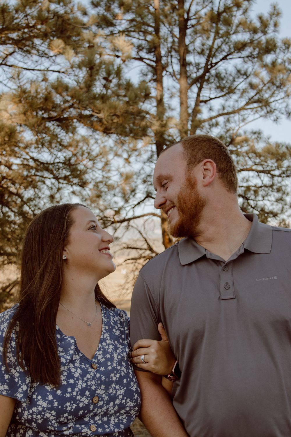 A romantic couple laughs together during a sunset photoshoot with pine trees in the background.