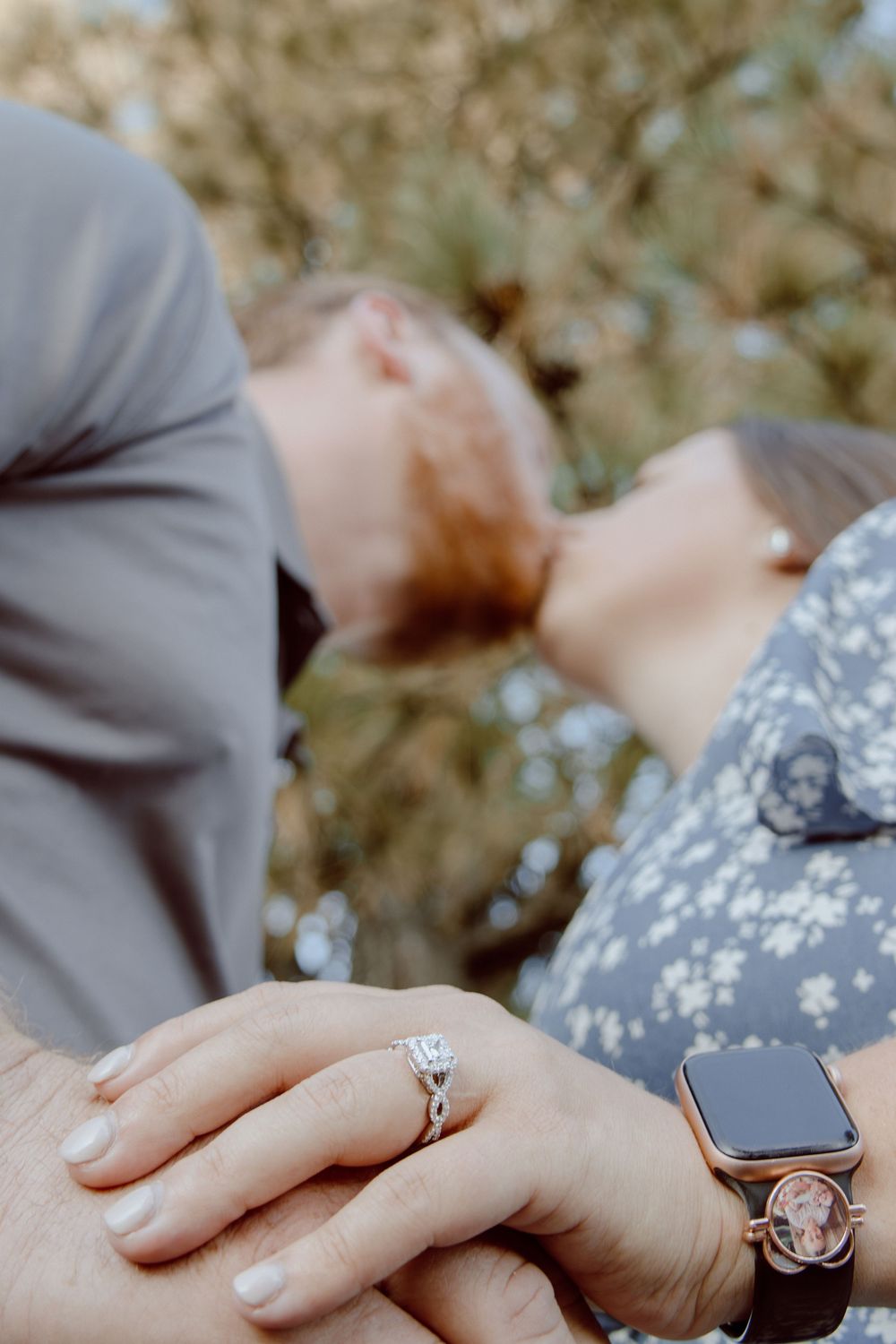 Close-up of hands showing an engagement ring and smartwatch against a soft blurred background.