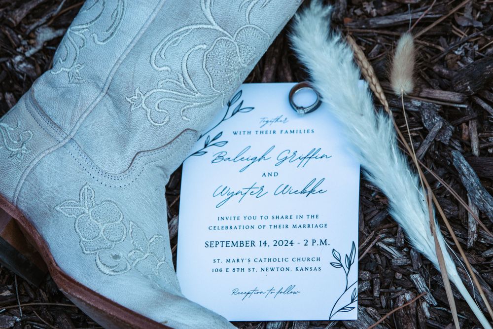 A wedding invitation with elegant calligraphy rests on textured fabric with a feather accent.