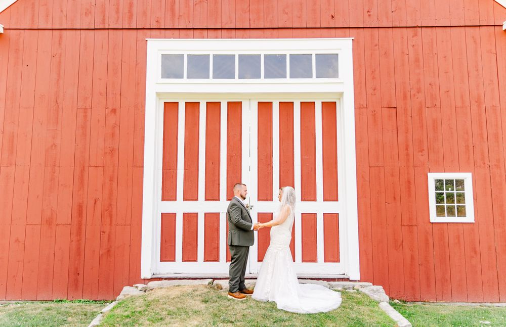 Wedding couple holding hands against large red and white barn door.