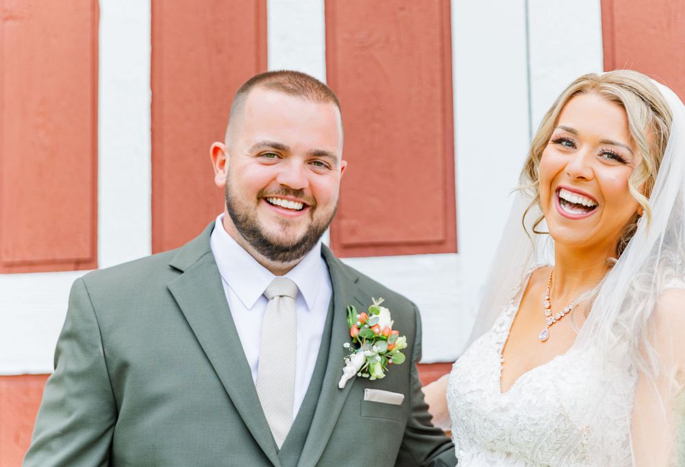 Happy newlyweds pose together against a red barn exterior.