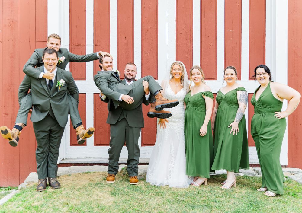 Wedding party striking fun poses in front of a red barn with white trim.