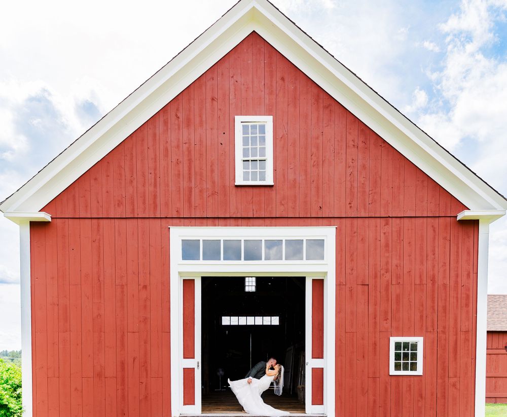 Classic farmhouse wedding photo with red barn and white trim doorway framing couple.