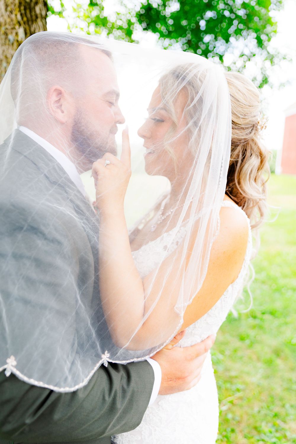 Romantic wedding couple embracing under veil with soft natural lighting.